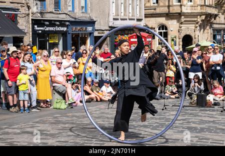 Royal Mile, Edinburgh, Schottland, Großbritannien, 9.. August 2022. Edinburgh Festival Straßenkünstler Fringe: Ein Mann spielt akrobatische Stunts auf einem cyr-Rad für die Menge im Sonnenschein Stockfoto