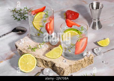 Kalter Sommer Erdbeer Cocktail Mojito, margarita, Daiquiri. Zwei Gläser mit frischem Erdbeersodagetränk, Eis und Barkeeper-Werkzeugen auf Travertin-Podiu Stockfoto