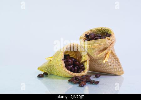 Sackleinen gefüllt mit gerösteten Kaffeebohnen auf weißem Hintergrund, Makrofoto Stockfoto