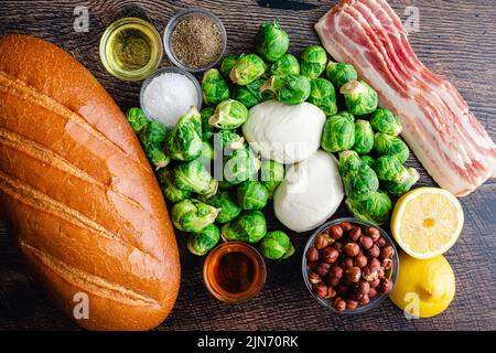 Karamellisierter Brüsseler Sprout-Toast mit Burrata & Bacon Zutaten: Frisches Brot, Rosenkohl und andere Zutaten auf Holzgrund Stockfoto