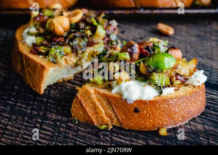 Karamellisierter Brüsseler Sprout-Toast mit Burrata & Bacon: Seitenansicht von geröstetem Brot mit Gemüse, Mozzarella-Käse und Speck Stockfoto