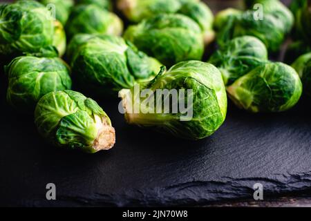 Nahaufnahme Blick auf frische Rosenkohl auf einem dunklen Stein Hintergrund: Seitenansicht von Rosenkohl auf einem rustikalen Schiefergestein Hintergrund Stockfoto