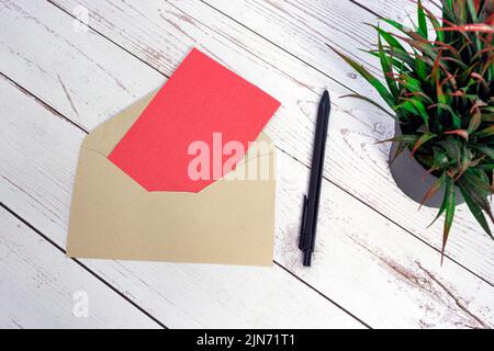 Rote Karte Mockup mit Umschlag, Stift und Topfpflanze auf Holztisch. Stockfoto