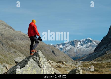 Rückansicht eines Touristen in roter Jacke und Kamera mit Blick auf Julier Pass, Schweiz Stockfoto