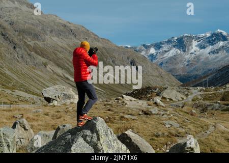 Rückansicht eines Touristen in roter Jacke und Kamera mit Blick auf Julier Pass, Schweiz Stockfoto