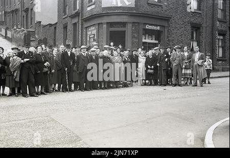 1950s, historisch, Busreise, Sheffield-Torquay Express, Passagieranzahl für Männer und Frauen auf der Straße in Grimesthorpe Rd, Pitsmoor in Sheffield, South Yorkshire, England, Großbritannien, Für ein Gruppenfoto vor der langen Reise nach Süden zum Badeort Torquay in Devon. Die meisten Männer und einige der Damen tragen Hüte. Es war eine Übernachtung, die am Freitag in Torquay am samstagmorgen wieder zurück nach Sheffield am Sonntag ging. Ein ziemliches Abenteuer für die OAPs! Hinter ihnen der steile Hügel der Ditchingham Road. An der Straßenecke, Lliy Bell's Lebensmittelgeschäft. Stockfoto