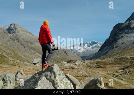 Rückansicht eines Touristen in roter Jacke und Kamera mit Blick auf Julier Pass, Schweiz Stockfoto