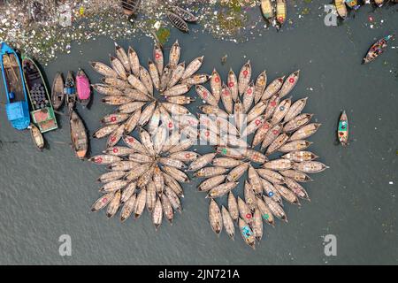 Dhaka, Bangladesch. 9. August 2022. Blick von oben auf Hunderte von Holzbooten, die wie Blumen im Hafen des Dhaka River aussehen, während sie sich um ihre Anlegestellen herum fächeln. Die Boote, die mit bunt gemusterten Teppichen geschmückt sind, sind bereit, Arbeiter aus den Außenbezirken der Stadt zu ihren Jobs im Zentrum zu transportieren. Der Buriganga-Fluss wird täglich als Route in die Stadt Dhaka für Millionen von Arbeitern genutzt. (Bild: © Mustasinur Rahman Alvi/ZUMA Press Wire) Stockfoto