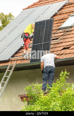 Zwei Männer installieren neue Sonnenkollektoren auf dem Dach eines Privathauses. Konzept für erneuerbare Energien. Installation von Photovoltaik. Energiesparend. Stockfoto