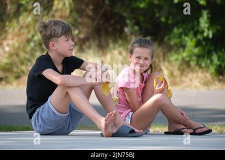 Junge hübsche Teenager Junge und hübsches Mädchen essen leckere reife Banane Naschen im Freien am Sommertag Stockfoto