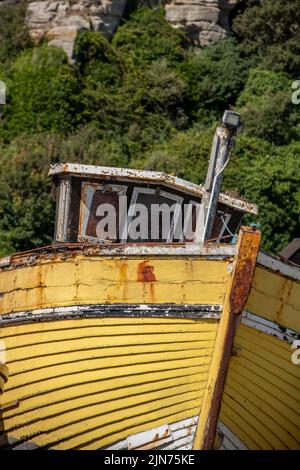 Alte gelbe Klinker baute hölzerne Fischerboot an Land am Strand bei hastings in kent hoch und trocken, alte veraltete hölzerne Fischerboot, schäbig schickes Boot Stockfoto