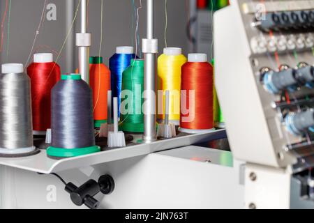 Spulen aus farbigen Fäden für industrielle Näh- und Stickmaschinen auf unscharfem Hintergrund. Speicherplatz kopieren. Nahaufnahme. Stockfoto