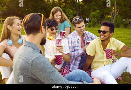 Eine Gruppe von Freunden trifft sich im Sommerpark und plaudern beim Picknick mit Pappbecher Kaffee oder Tee. Stockfoto