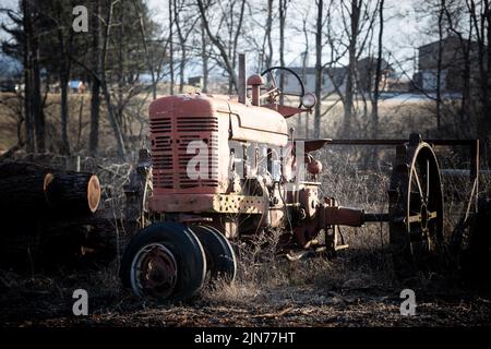 Eine Nahaufnahme eines alten roten Traktors, der auf einem Feld in der Nähe der Farm unter der Sonne geparkt ist Stockfoto