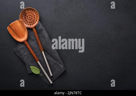 Kochgeschirr aus Holz, Basilikumblätter und Gewürze auf dunklem Steingrund. Abstrakter Lebensmittelhintergrund. Draufsicht auf dunklen rustikalen Küchentisch mit Holz Stockfoto