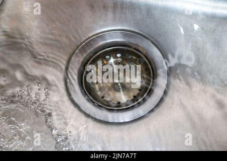 Waschbecken aus Edelstahl mit Ablaufstopfen und fließendem Wasser - Nahaufnahme Stockfoto