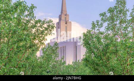 Panorama Puffy Wolken bei Sonnenuntergang Betonweg mit Säulenbäumen auf beiden Seiten, die zur Kirche führen. Gehweg zur eingezäunten Kirche mit hohem Kirchturm Stockfoto