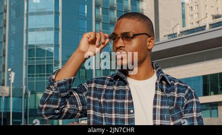 Porträt des Mannes in der Stadt afroamerikaner junger Student Mann in stilvoller Sonnenbrille trägt kariertes Hemd sieht weg zu Seite träumen Denken Stockfoto