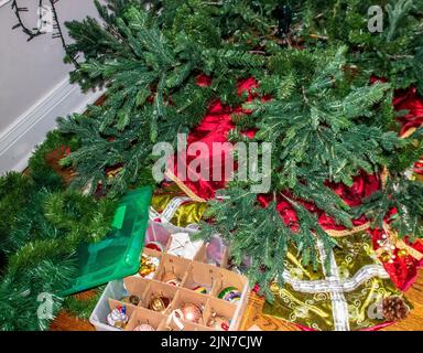 Den Baum nach den Feiertagen abbauen - einen künstlichen Baum mit Lichtern und Vintage-Ornamenten in einer Aufbewahrungsbox demontieren. Stockfoto