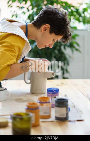 Junge weibliche Keramiker schmücken Töpfer Krug nach dem Brennen. Handwerkliche Keramik in Keramik-Werkstatt Stockfoto