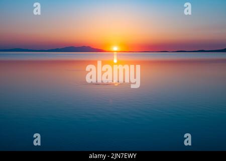 Runde Wassertröpfchen in Ringen über dem Wasser bei Sonnenuntergang. Wasser tropft, wirbelt und spritzt. Wellen auf Meer Textur Muster Hintergrund. Stockfoto