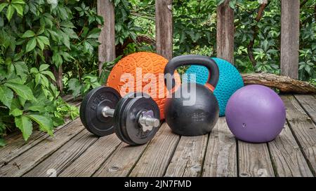 Drei schwere Slam-Kugeln, Eisen-Kugelhantel und Hantel auf einem Hinterhof-Deck, Heim- und Hinterhof-Fitnessstudio-Konzept Stockfoto