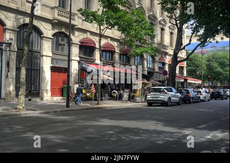 Paris, Frankreich - 26. Mai 2022: Straßencafés mit Fußgängern und Fahrzeugen im Vordergrund Stockfoto