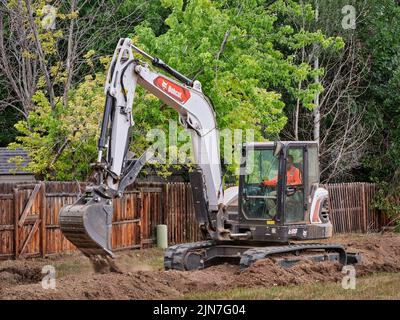 Fort Collins, CO, USA - 21. Juli 2022: E88, der größte Bobcat Kompaktbagger, der in einem Wohngebiet entlang des Hinterhofzauns arbeitet. Stockfoto