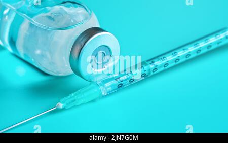 Glasfläschchen mit klar flüssiger und hypodermischer Spritzennadel in der Nähe von Details aus Cyan Stockfoto