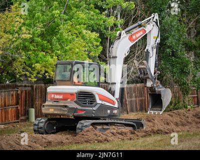 Fort Collins, CO, USA - 21. Juli 2022: E88, der größte Bobcat Kompaktbagger, der in einem Wohngebiet entlang des Hinterhofzauns arbeitet. Stockfoto