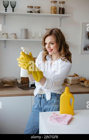 Ein Mädchen in gelben Handschuhen hält ein Reinigungsspray auf dem Hintergrund der Küche Stockfoto