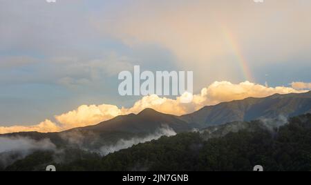 Ein Sonnenuntergang mit einem Regenbogen und großen geschwollenen Wolken im Great Smoky Mountain National Park. Nach einem schweren Sturm verharmt Rauch in den Bergen. Stockfoto