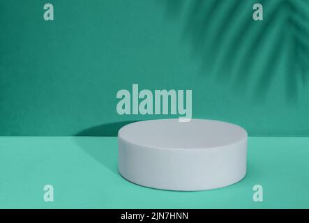 Weißes Podium im Hintergrund. Vorlage, Modell für Präsentationsprodukte. Komposition im grünen Stil mit tropischem Palmenblatt-Schatten. Stockfoto