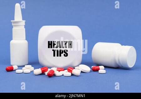 Medizinisches Konzept. Auf der blauen Oberfläche der Pille, Kapsel, Spray, Glas und Würfel mit der Aufschrift - GESUNDHEITSTIPPS Stockfoto