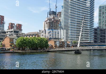 Die South Quay Footbridge an einem sonnigen Tag in Canary Wharf mit Bauarbeiten für neue Wohngebäude in der Ferne. London - 9.. August 2022 Stockfoto