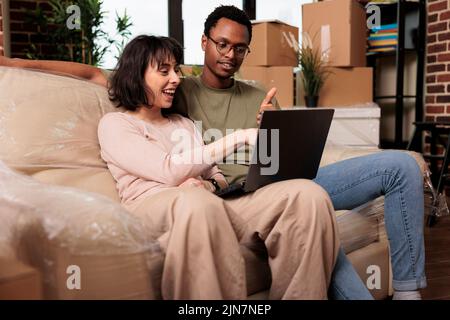 Diverse Paar tun Online-Shopping auf Laptop, um Möbel zu kaufen, Surfen im Internet Website für Wohnkultur Inspiration. Umzug in gemietete Wohnung Eigentum zusammen für Beziehung Veranstaltung. Stockfoto