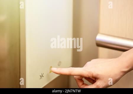 Sie drückt mit ihrem Zeigefinger auf die Stockwerks-Nummer, die im Aufzug digital angezeigt wird. Stockfoto