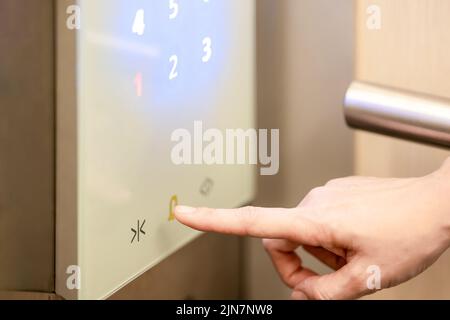 Sie drückt mit ihrem Zeigefinger auf die Stockwerks-Nummer, die im Aufzug digital angezeigt wird. Stockfoto