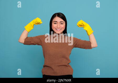 Glücklich energetisch schöne asiatische Hausfrau heben Arme und zeigen Bizeps isoliert blauen Hintergrund, Hausfrau Arbeiter, Reinigung nach Hause Konzept, Weibliche lächeln nach Abschluss seiner Arbeit, Stockfoto