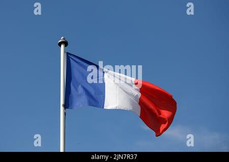 Französische Flagge flattert im Wind mit blauem Himmel Hintergrund. Tricolor auf einem weißen Fahnenmast Stockfoto