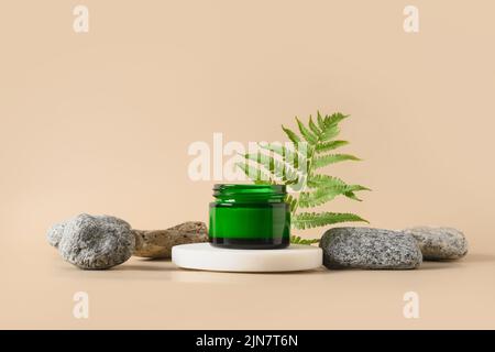 Podium für Kosmetikprodukte in moderner Komposition mit tropischen Farnblättern und Steinen auf beigem Hintergrund. Stockfoto