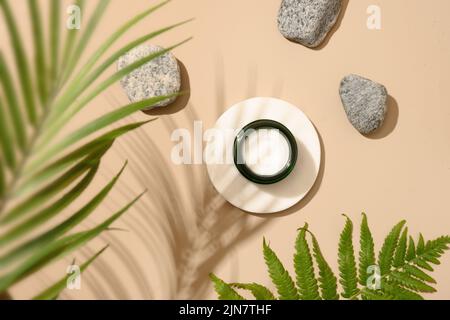 Podium für Kosmetikprodukte in moderner Komposition mit tropischen Farnblättern und Steinen auf beigem Hintergrund mit Schatten. Blick von oben. Stockfoto