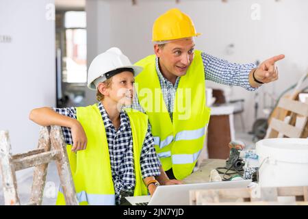 Der junge Junge und sein Vater besprechen den Arbeitsplan in einer neuen Wohnung Stockfoto