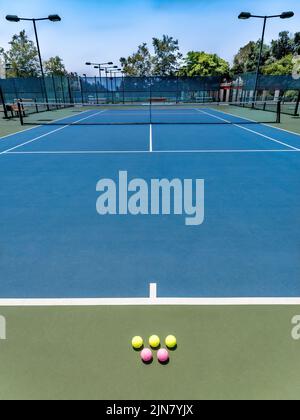 Rosafarbener Tennisball auf dem blauen Vorplatz eines Tennisplatzes an einem sonnigen Tag. Stockfoto