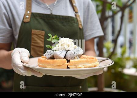 Frau hält belgische Waffeln mit Drachenfrucht und Eis auf einem Teller Stockfoto