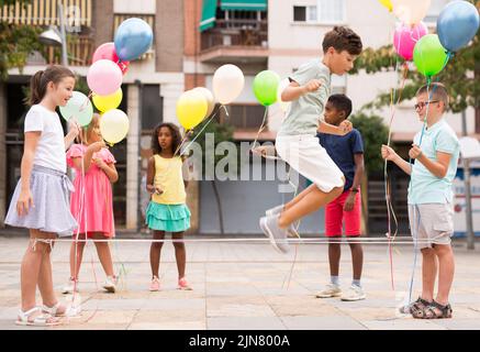 Glückliche Jugendliche mit Luftballons, die im Innenhof an einem chinesischen Springseil springen Stockfoto