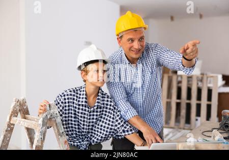 Ein Architekt und ein Junge verwenden einen Laptop, während sie über den Arbeitsprozess im Haus sprechen, der gerade renoviert wird Stockfoto