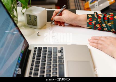 Defcous weibliche Hand schreiben mit Stift. Unkenntlich elegante Frau, die im Büro am Computer arbeitet. Beginn oder Ende eines Arbeitstages. Arbeitsbereich. Draufsicht. Ti Stockfoto