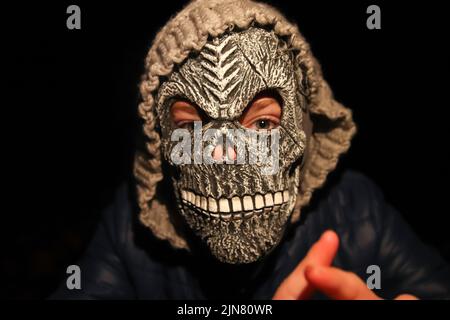 Unschärfen Sie Halloween-Menschen. Person in grimmiger Reaper Maske auf schwarzem Hintergrund stehend. Dunkle Nachtstimmung, Alptraum. Halloween-Horror. Schädelgeist. Hände Fr. Stockfoto