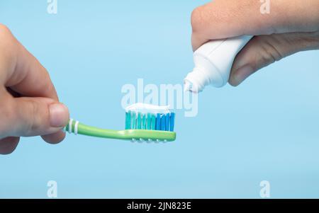 Zahnpasta wird auf die Zahnbürste aufgetragen, Zähneputzen in der Hand auf blauem Hintergrund. Stockfoto